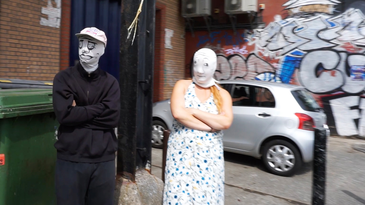 masked figures stand with hostile body language against graffiti